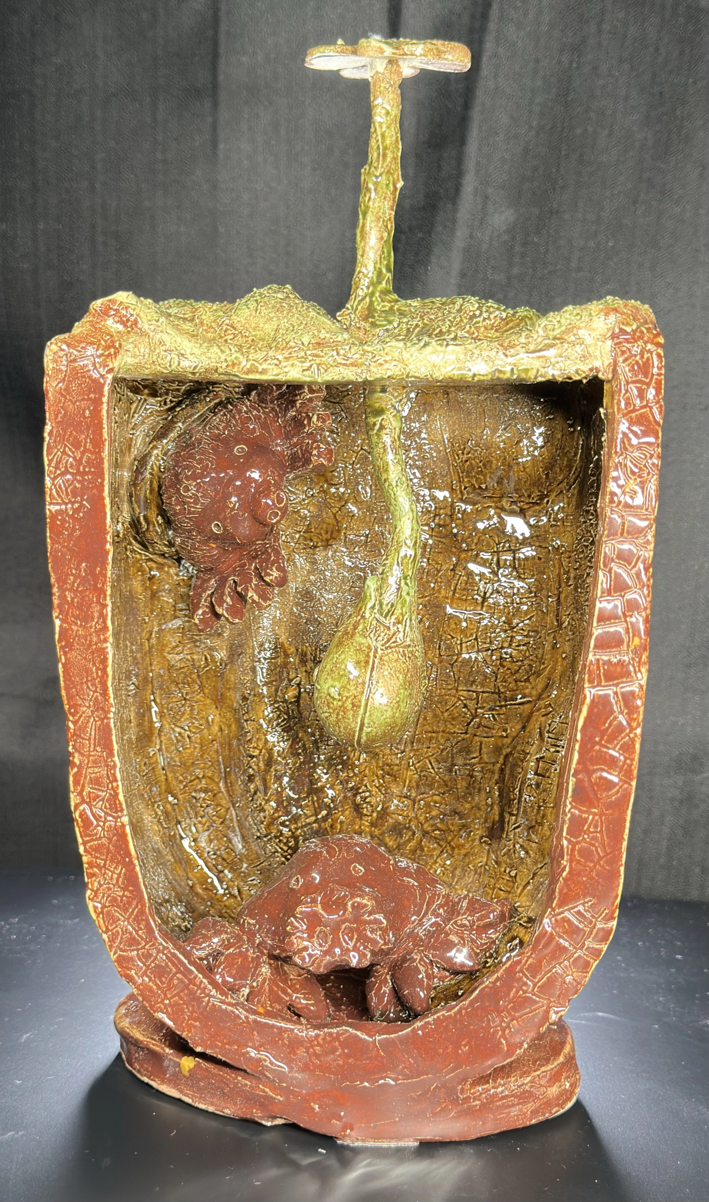 Moles Underground Shadow Box: a glazed ceramic scene in a red-orange rectangular frame showing a flower and bulb above ground, a red mole-like animal hanging at left, and another animal in the textured underground below.
